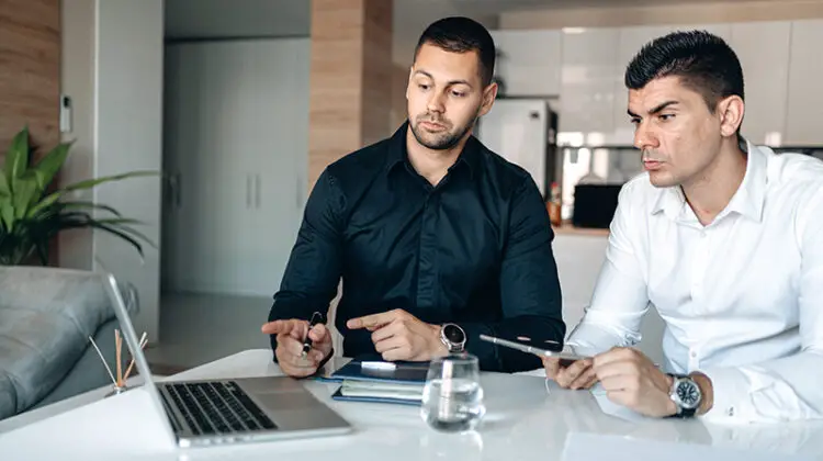 two businessmen having conversation holding pen and macbook pro