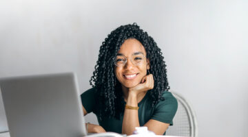 Happy ethnic woman sitting at the table with laptop