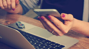woman using iPhone with her laptop on the table