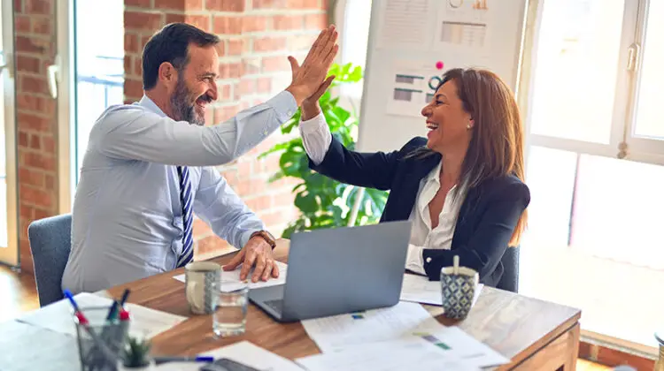 Two middle age business workers with smile on face hand giving high five at the office