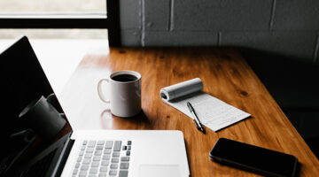Laptop, white ceramic mug, and smartphone on top of wooden table