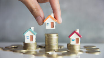 Three Miniature house on top of pile of coins