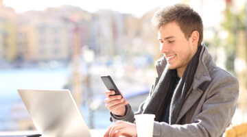 Young man smiling while using his mobile phone and laptop