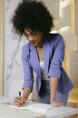 Businesswoman in blue blazer standing while writing on the desk
