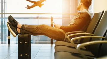 Man sitting on airport lobby with feet on luggage