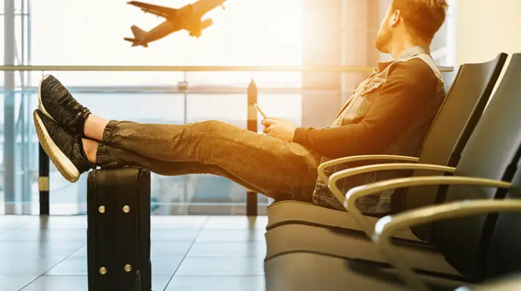 Man sitting on airport lobby with feet on luggage
