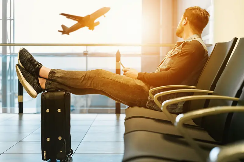 Man sitting on airport lobby with feet on luggage