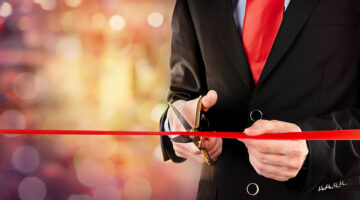 Businessman cutting red ribbon with pair of scissors