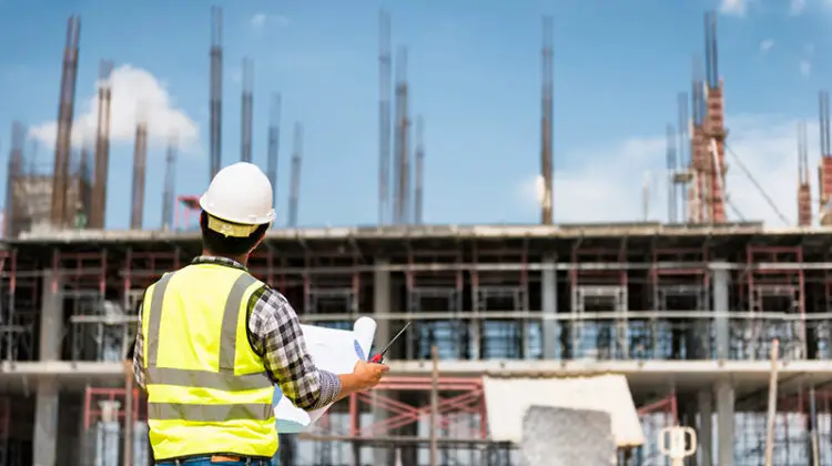 Engineering Consulting People on construction site holding blueprint in his hand.