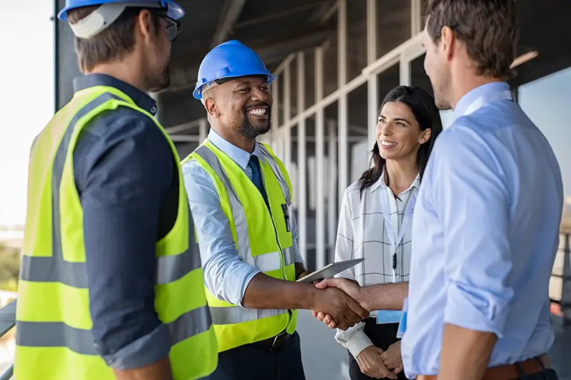 Smiling engineer shaking hands at construction site with happy architect