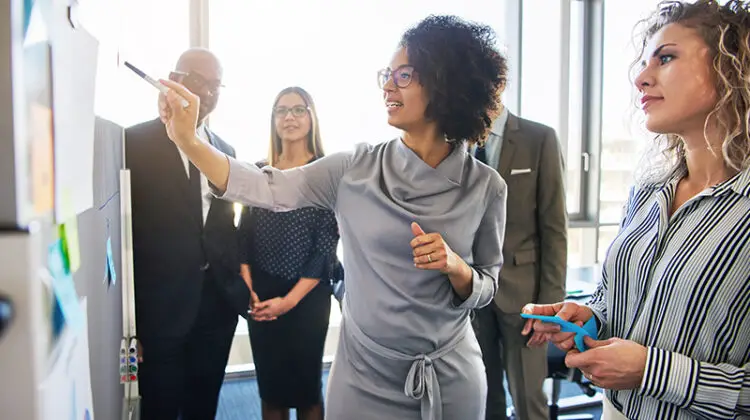 Diverse group of focused businesspeople brainstorming together on a whiteboard during a strategy session