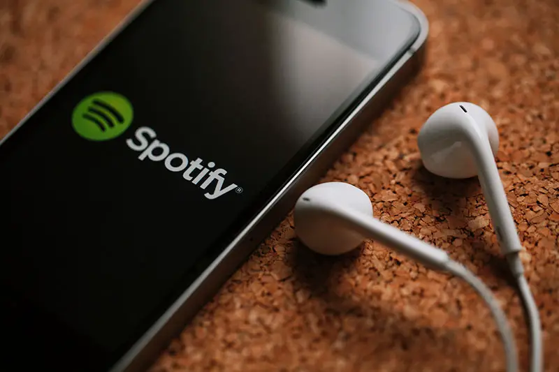 Close up of mobile phone with Spotify logo in the screen and white earphones