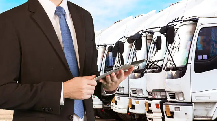 Businessman holding tablet standing over trucks in a row with Container background