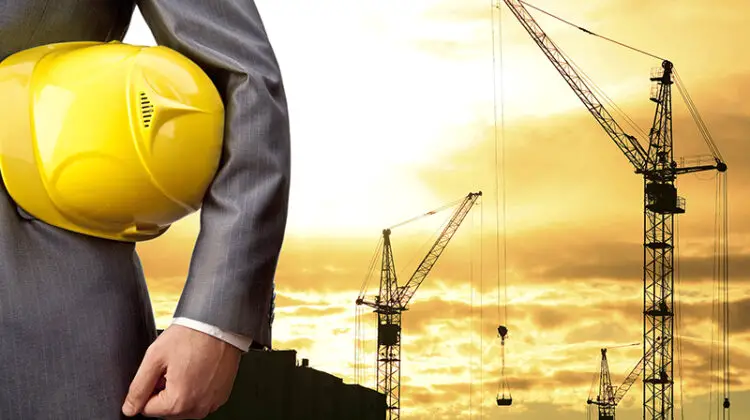 Businessman holding yellow helmet with construction site on the background