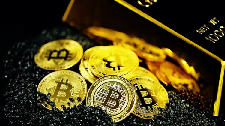 Bitcoins beside gold bar with black sand