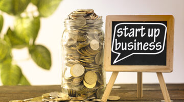 saving jar full of coins and mini blackboard with text start up business