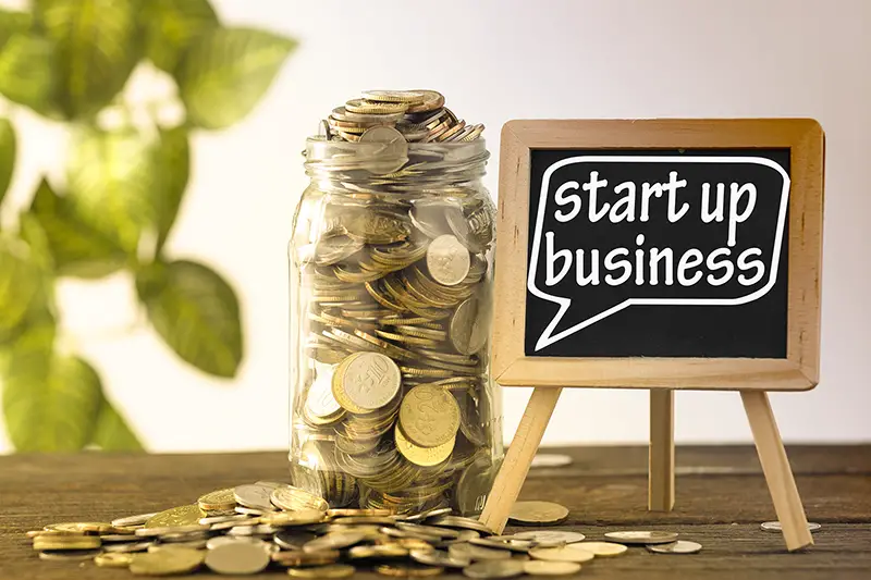 saving jar full of coins and mini blackboard with text start up business