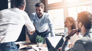 Young modern men in smart casual wear shaking hands and smiling while working in the office