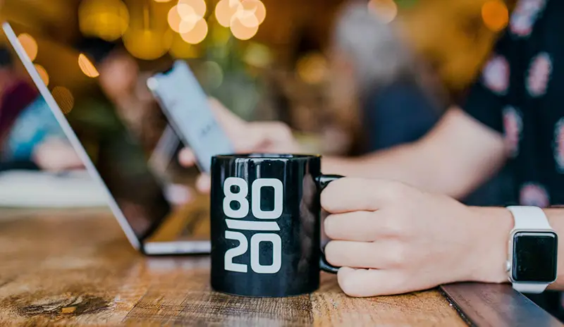 Person holding black coffee mug with  80/20 number printed