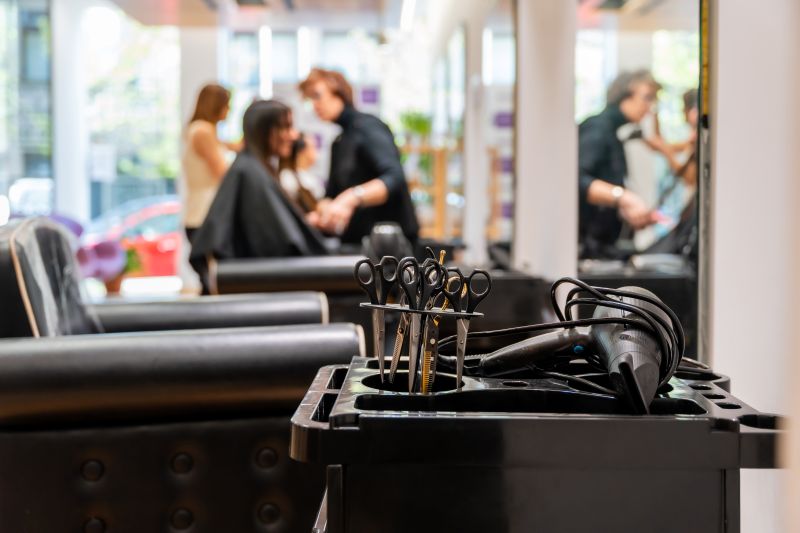 Hairdressing scissors and a hair dryer on a salon trolley, with stylists working with clients in the background.