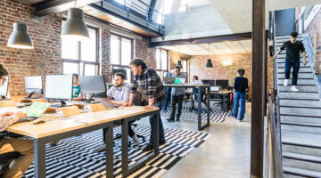Man standing beside another man sitting while using computer