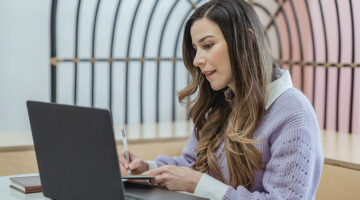 positive woman writing on notebook and watching laptop