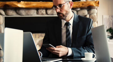 Businessman in black suit using his mobile phone and laptop in the office