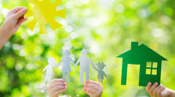 Ecology house and family in hands against spring green background