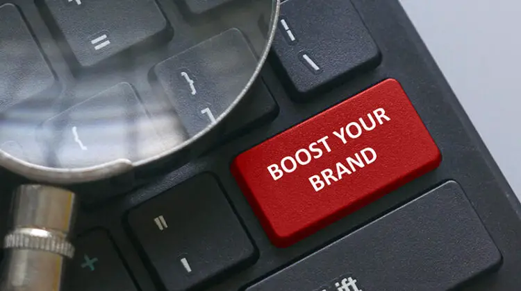 Magnifying glass on a computer keyboard with red button written with advice Boost your brand.