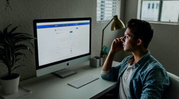 Man in blue denim jacket facing turned on monitor