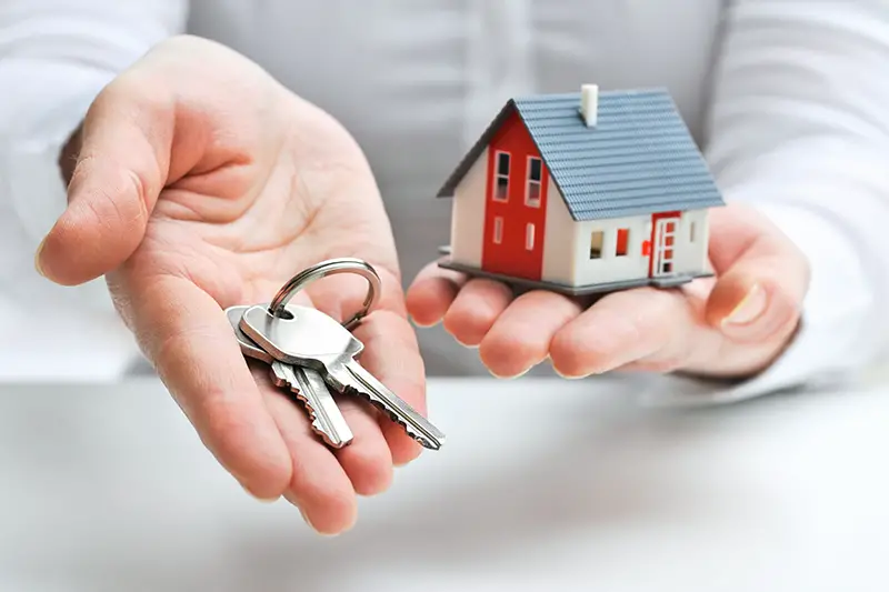 Person holding house miniature and a house key
