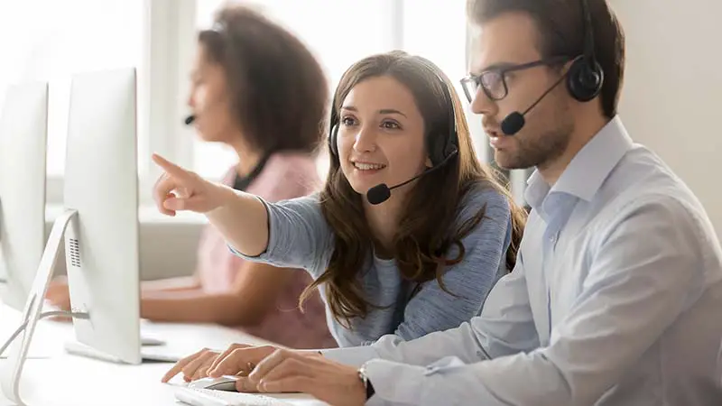 Female call center agent operator telemarketer helping male colleague
