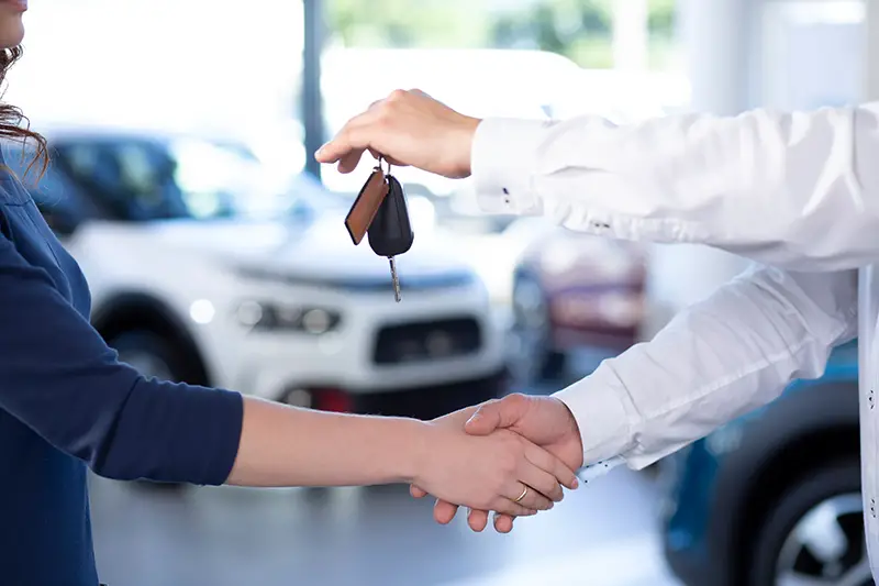Close-up of car dealer shaking buyer's hand and giving keys after transaction