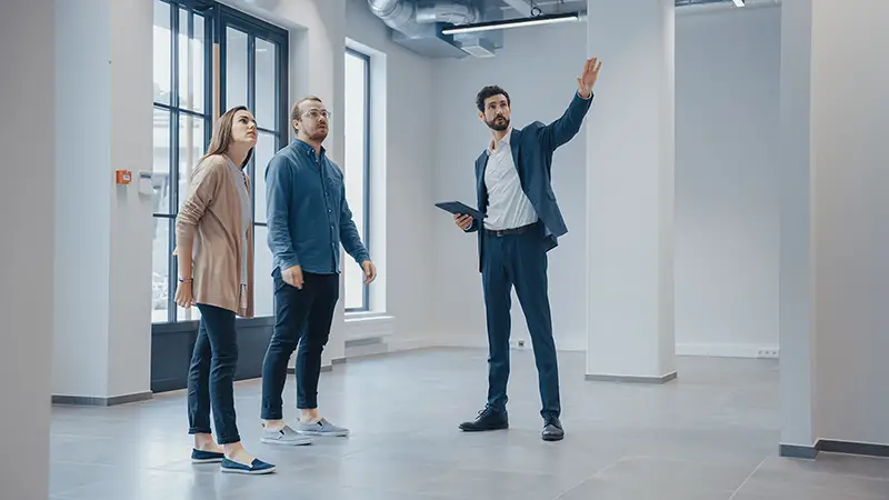 Real Estate Agent Showing a New Empty Office Space to Young Male and Female Hipsters. 