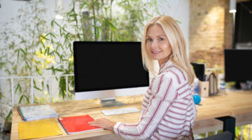 Blonde woman sitting at desk in front of screen