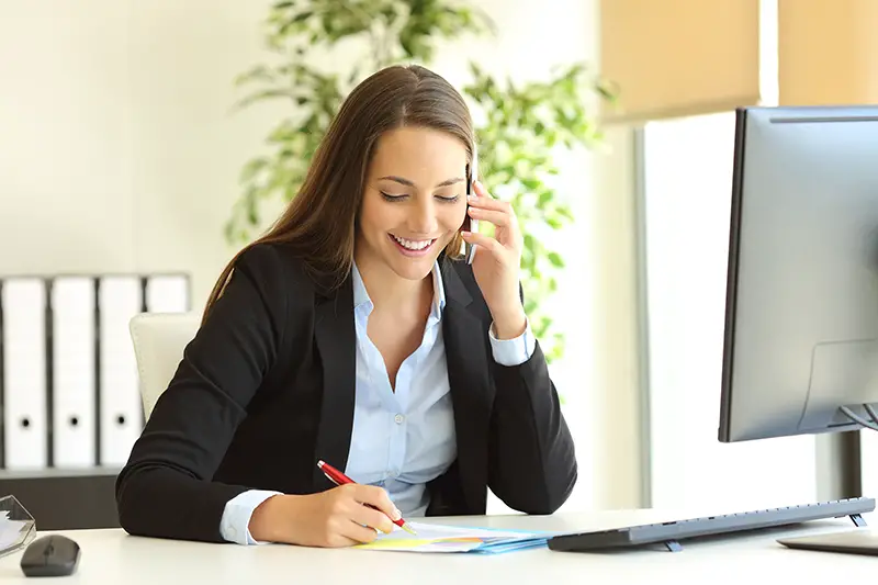 businesswoman calling on mobile phone and taking notes on a desk