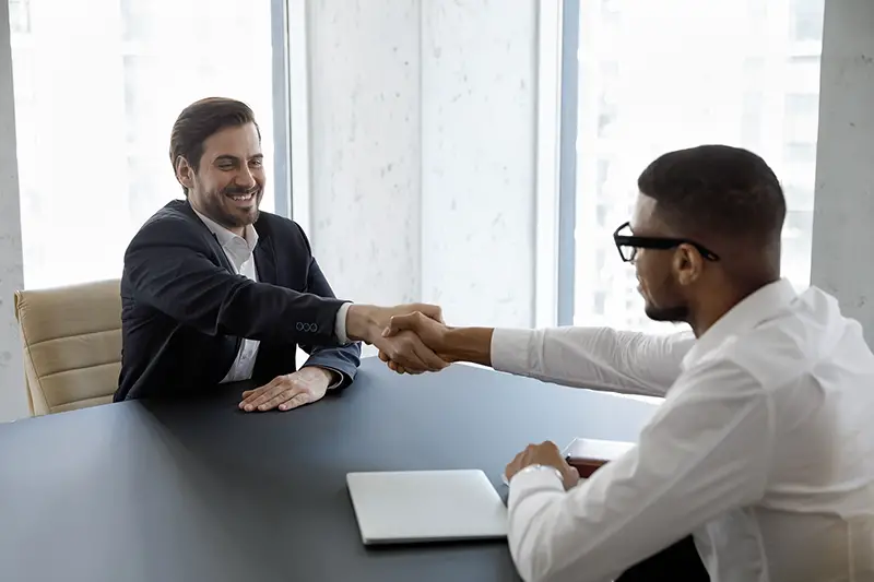 Happy young male vacancy candidate shaking hands with African American hr manager
