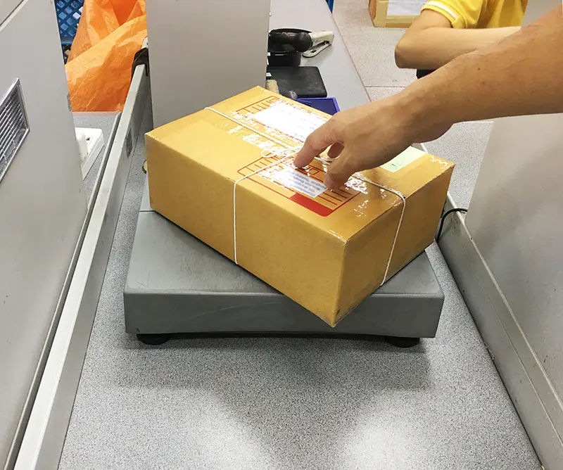 A man sending a box on parcel scale for delivery at counter service post office