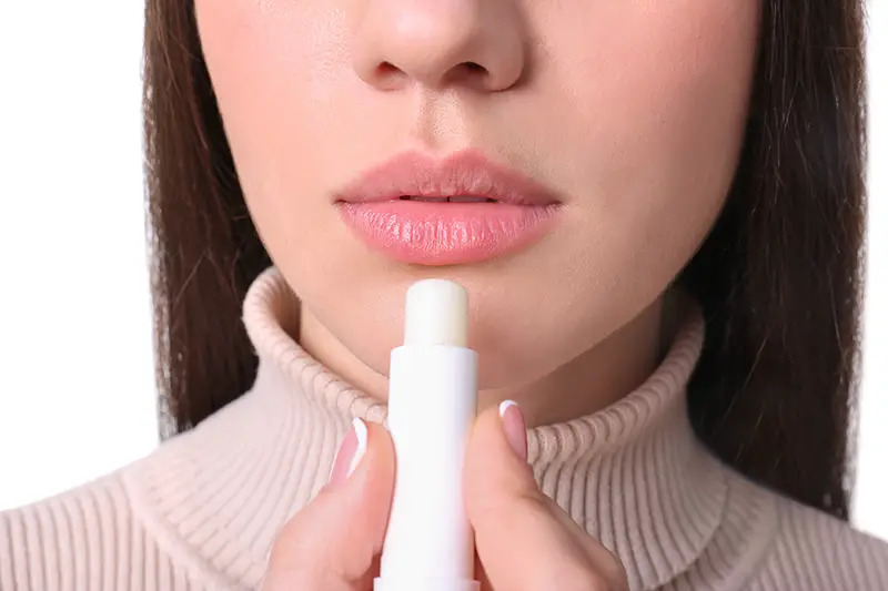 Young woman applying cold sore balm on lips