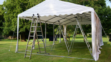 event tent set up with ladders on the lawn in a park