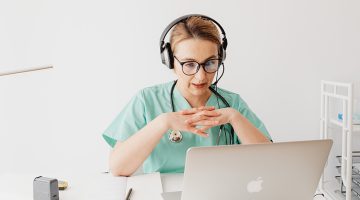 woman in scrub suit sitting in front of a laptop on a video call