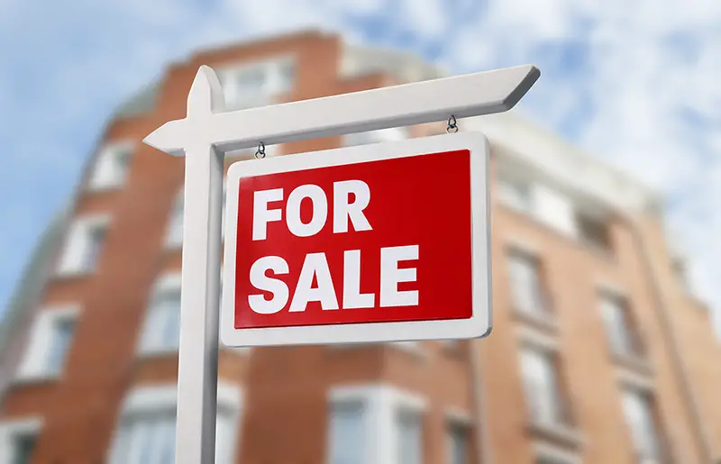 Sign FOR SALE in front of modern apartment house outdoors