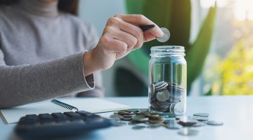Woman putting coins in a glass jar for savings