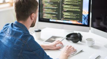 Back view portrait of contemporary web developer writing code for program sitting at desk and working on startup project in modern office, copy space