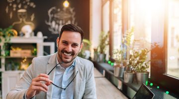 Portrait of a successful entrepreneur holding eyeglasses while sitting at the cafe in front of a laptop.