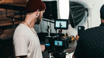 Man in white polo shirt standing in front of black video camera