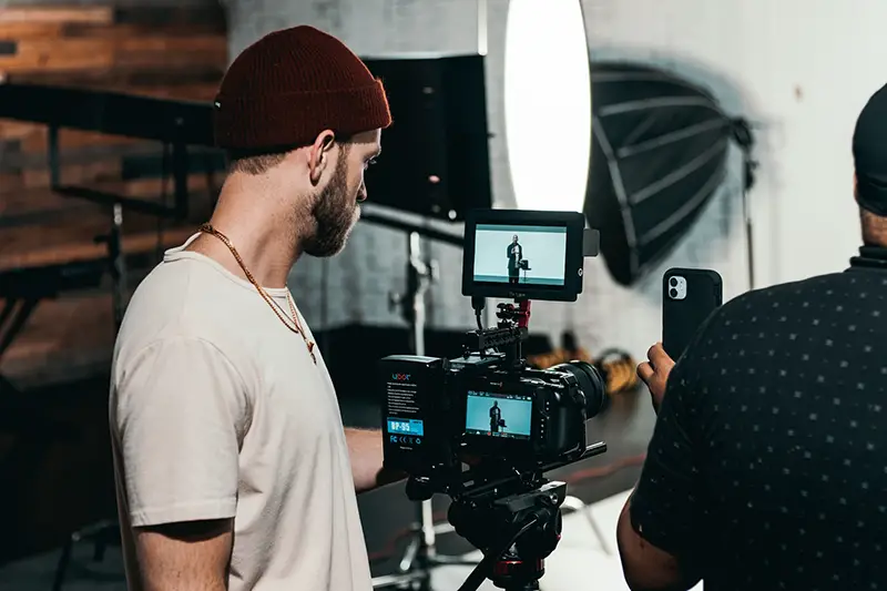 Man in white polo shirt standing in front of black video camera