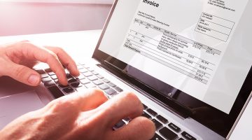 Close-up Of Businessman's Hands Working On Invoice On Laptop At Office