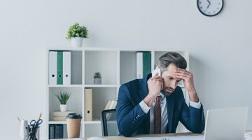 Upset businessman touching his forehead while talking on his phone at work