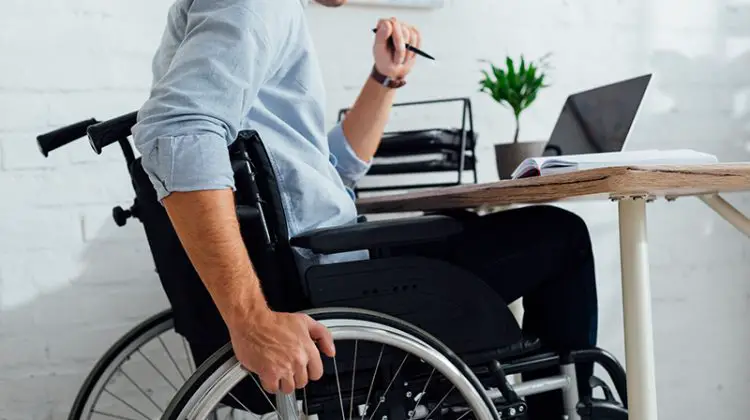 Disabled man sitting on his wheelchair in front of his laptop